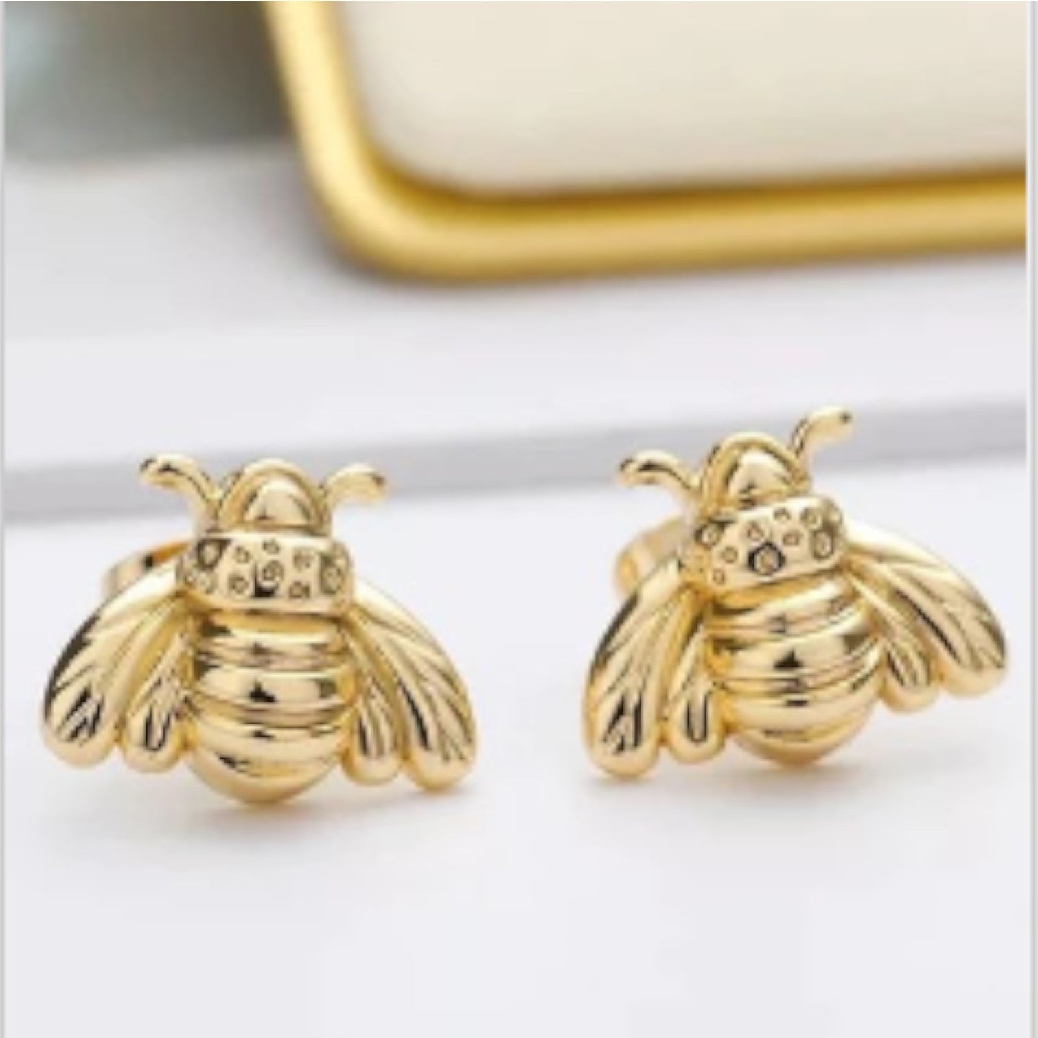 Gold bee-shaped earrings on a white surface.