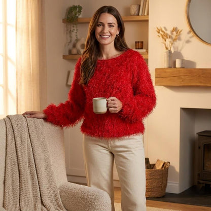 A smiling woman in a bright red sweater holds a mug in a cozy living room.