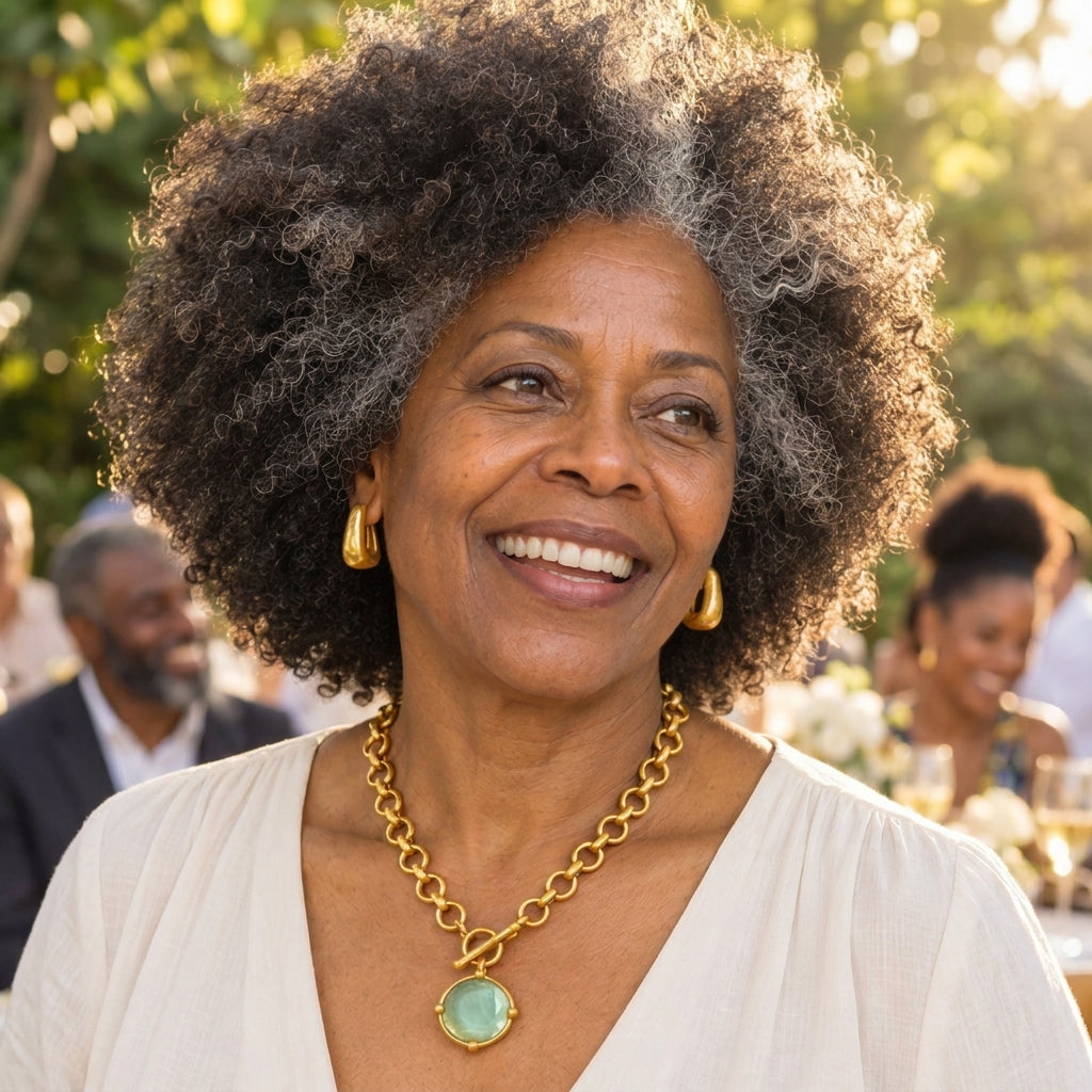 Smiling woman in a garden setting, wearing gold jewelry.