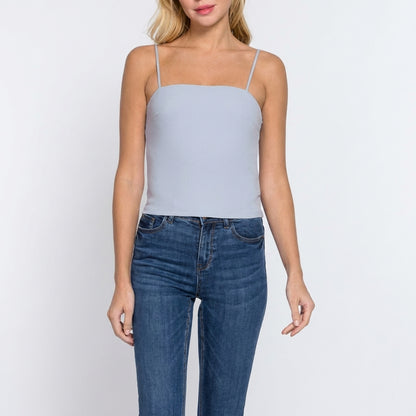 Woman in a light blue tank top and jeans on a plain background.