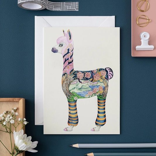 Colorful alpaca illustration on a card surrounded by stationery items.