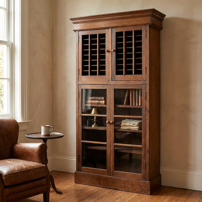 Wooden cabinet with books and lamp, next to a leather chair by a window.