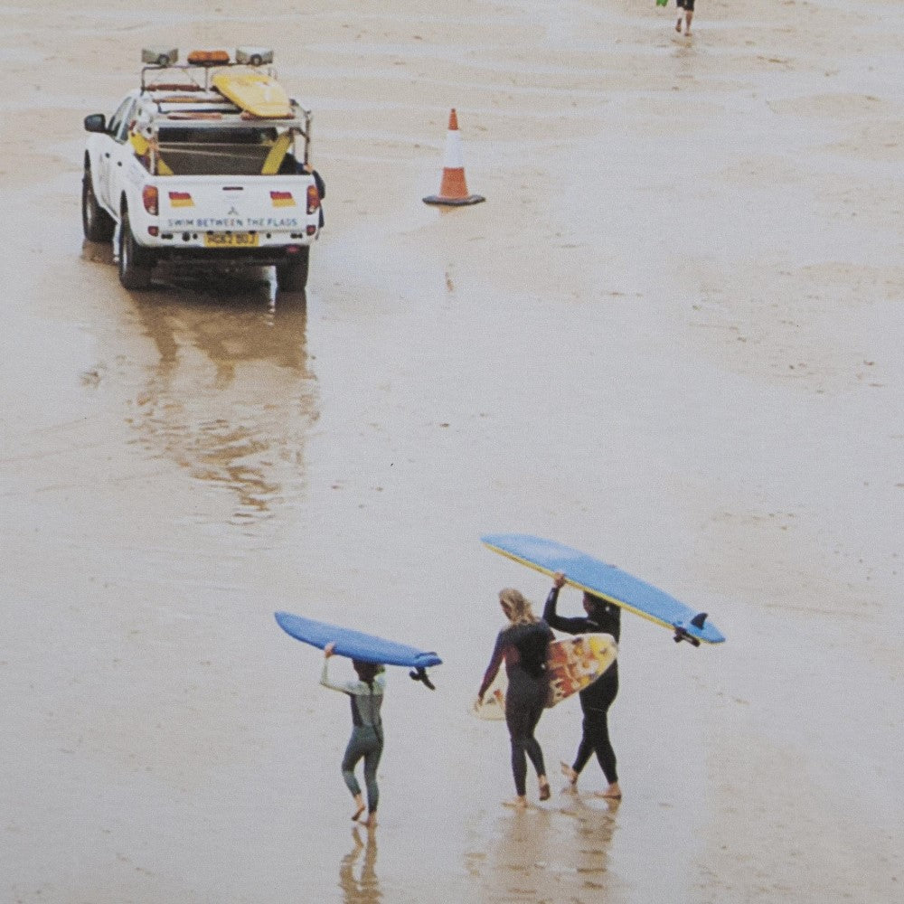 Surfers and vehicle on a sandy beach.