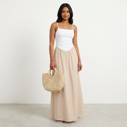 Woman in white top, striped skirt, holding a woven handbag.