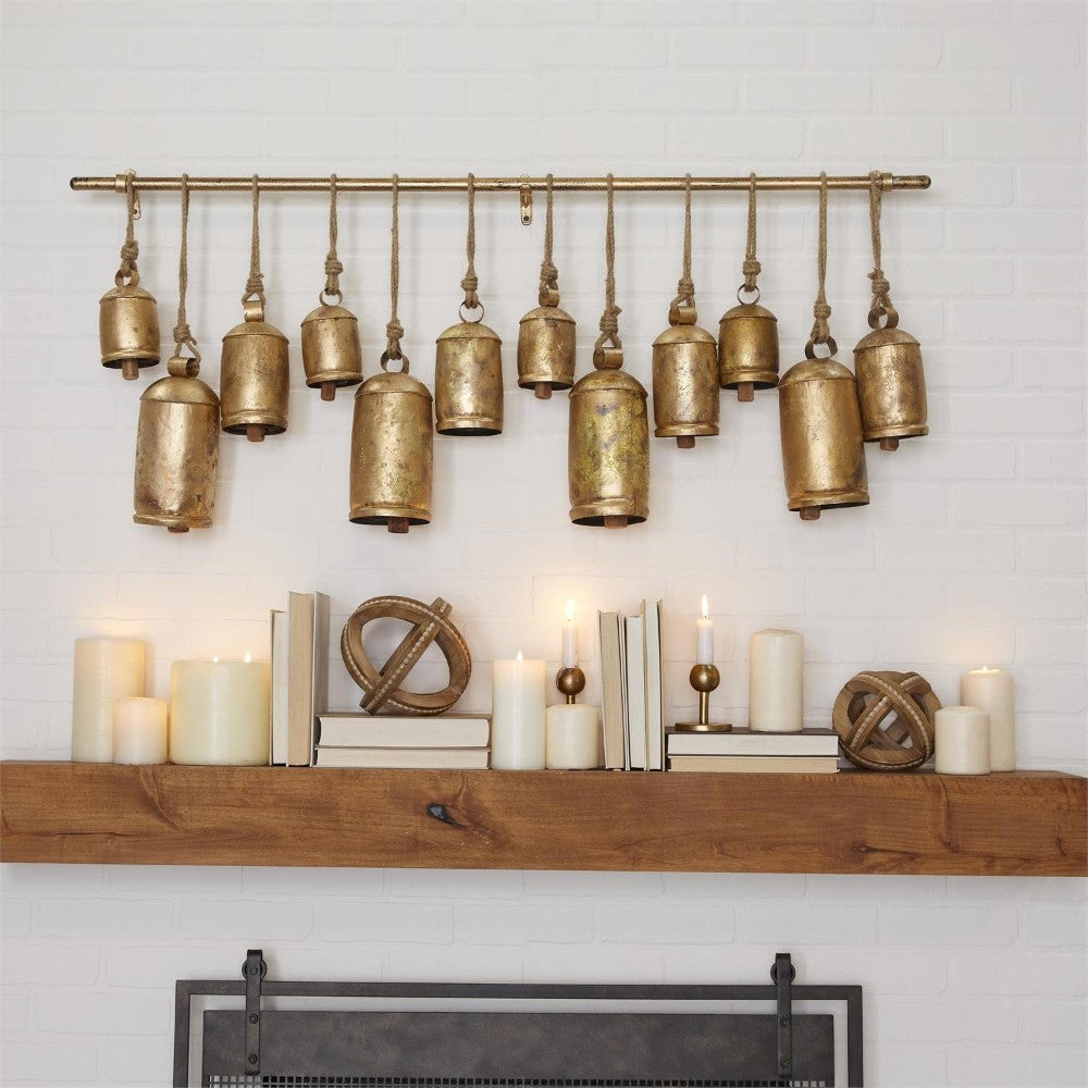 Rustic bells and candles decorate a wooden mantel against a white brick wall.