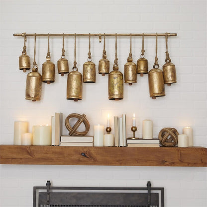 Rustic bells and candles decorate a wooden mantel against a white brick wall.