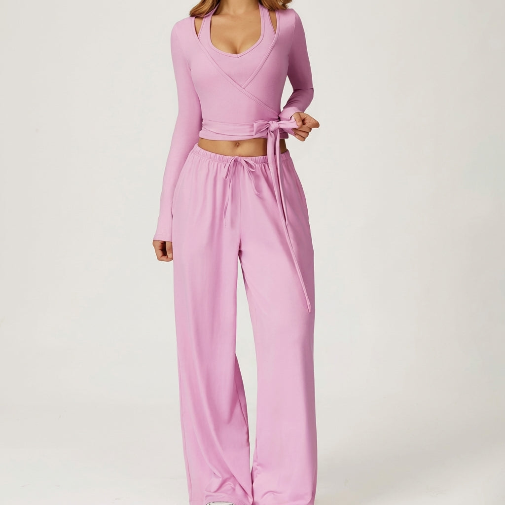Person in pink wrap top and loose pants with a bow, posed on a neutral background.