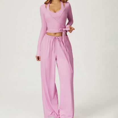 Person in pink wrap top and loose pants with a bow, posed on a neutral background.