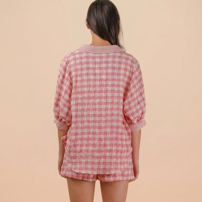 Person in pink checkered outfit standing against a beige background, seen from behind.