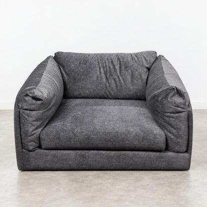 A gray, plush armchair on a plain floor.