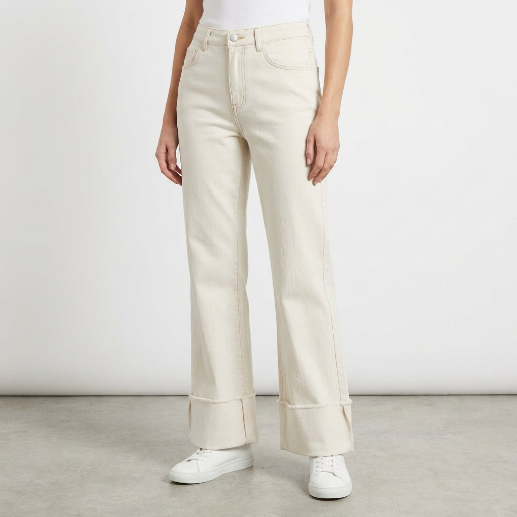 Woman in creamy wide-leg jeans and white sneakers on a plain background.