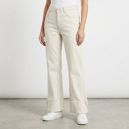Woman in creamy wide-leg jeans and white sneakers on a plain background.