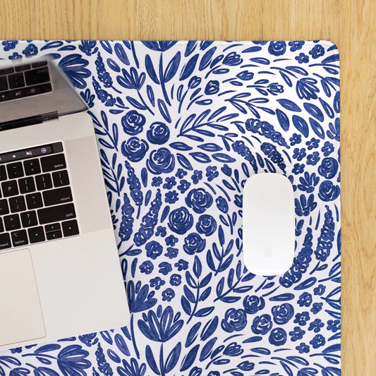 Laptop and mouse on a blue floral mousepad on a wooden desk.