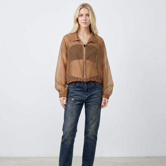 Woman in a sheer brown top and jeans, standing against a plain backdrop.