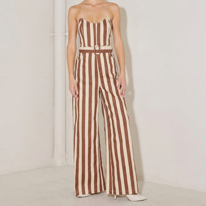 Person in a striped brown and cream jumpsuit, standing against a white wall.