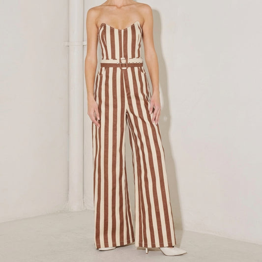 Person in a striped brown and cream jumpsuit, standing against a white wall.