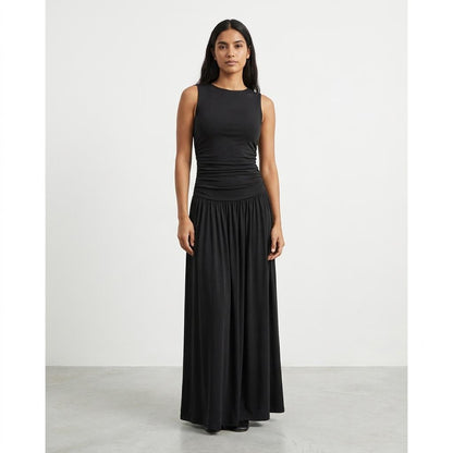 Woman in a sleeveless black dress stands against a plain white background.