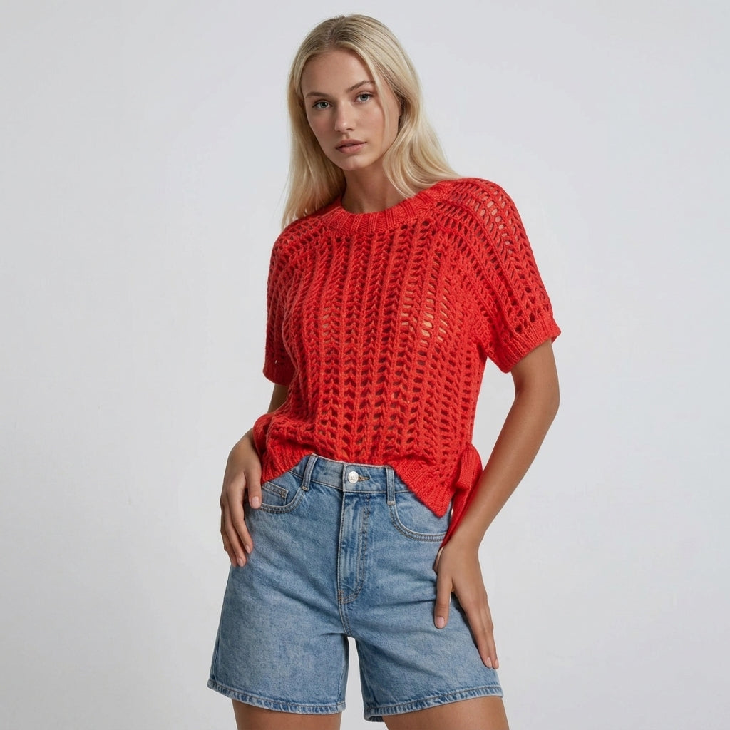 Person in a red knit top and denim shorts poses confidently.