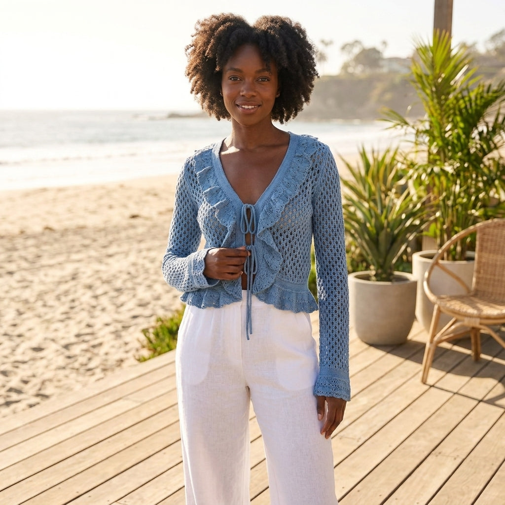 Smiling person in blue crochet top and white pants on a sunny beachside deck.