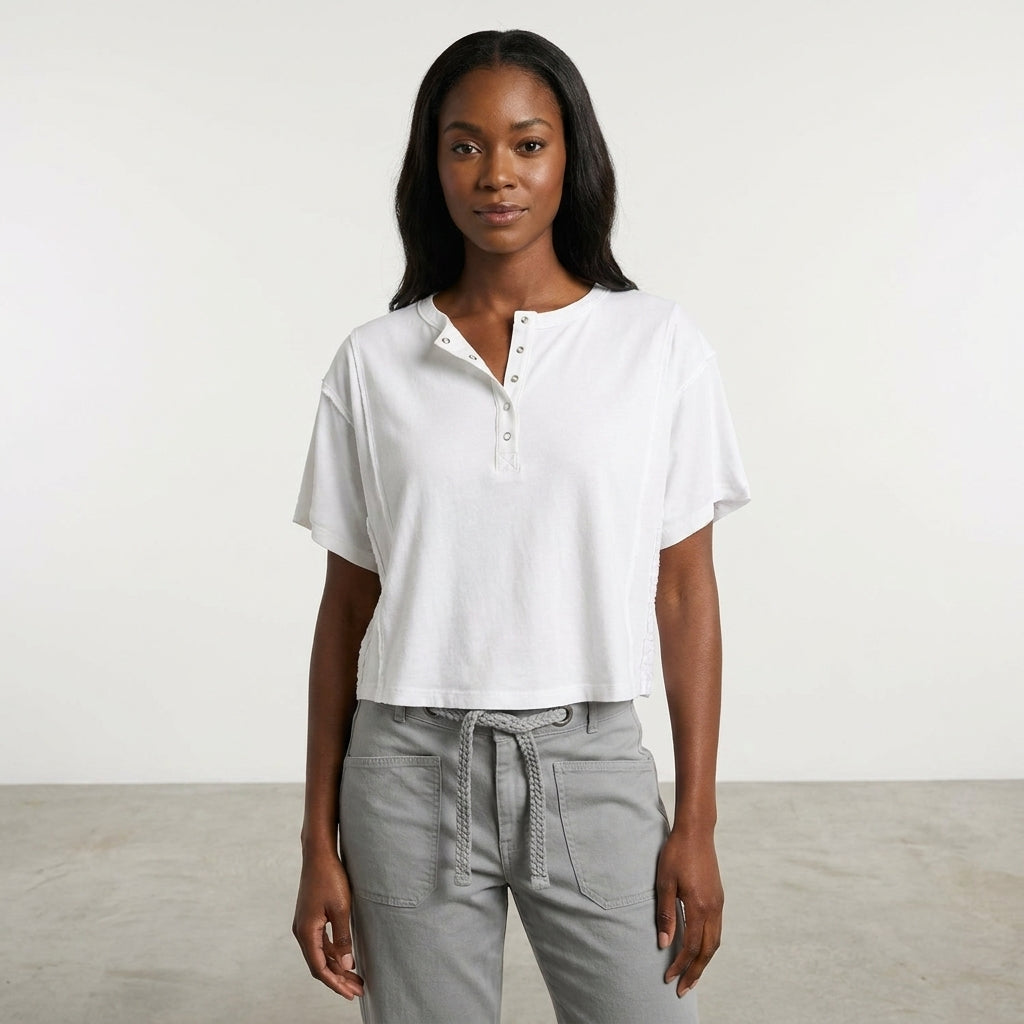 Woman in a white buttoned top and grey pants stands against a plain background.