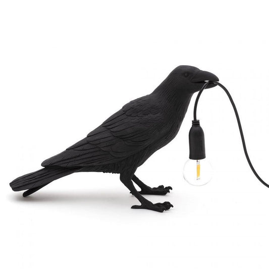 Black bird lamp holding a bulb in its beak.