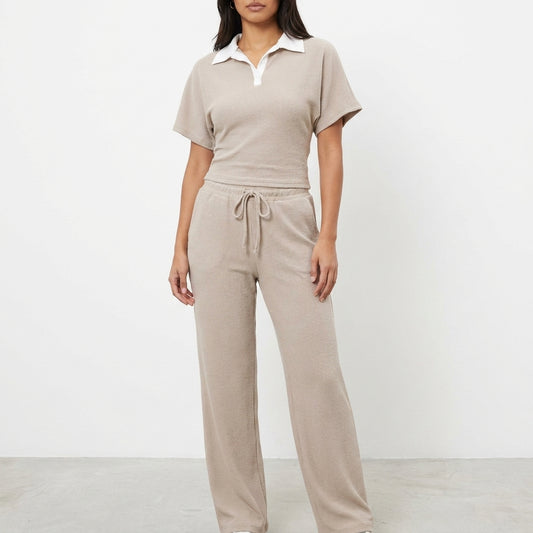 Woman in beige loungewear with collared top, standing against white background.