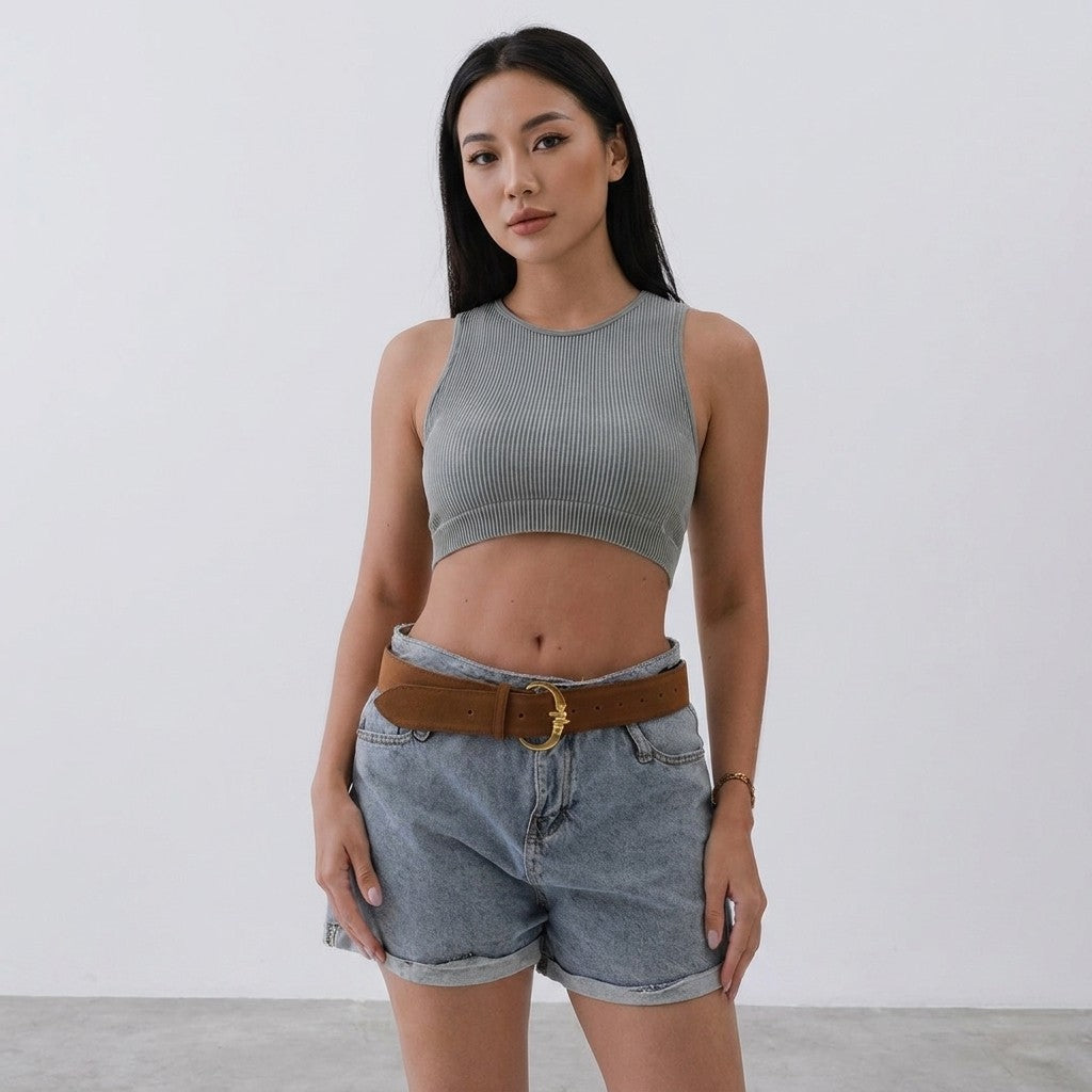 Woman in a crop top and denim shorts stands against a plain background.