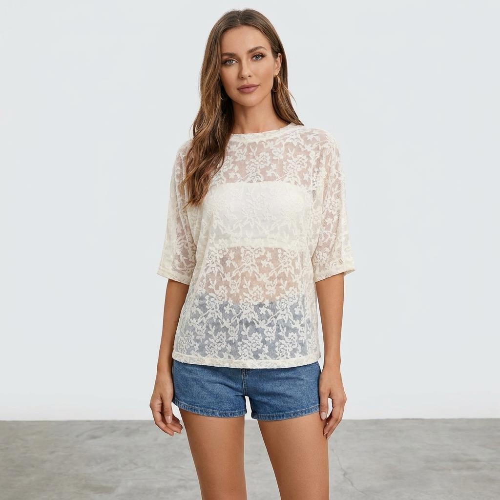 Woman in lace top and denim shorts standing in a minimalistic setting.
