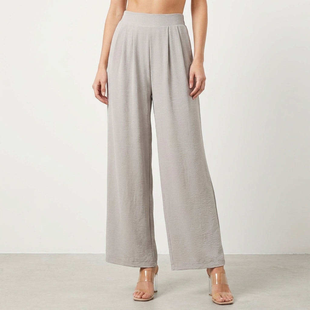 Model in gray wide-leg pants and clear heels, on a neutral background.
