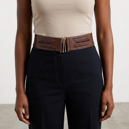 Woman wearing a tan top and brown belt with black pants.