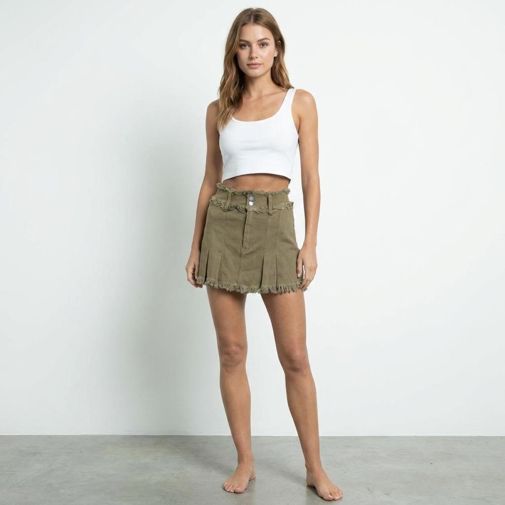 Woman in white tank and olive skirt stands barefoot against white background.