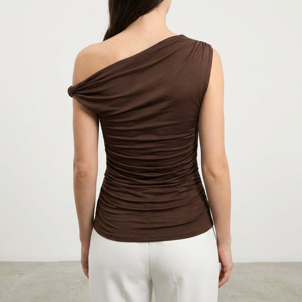 Woman in a one-shoulder brown top, white pants, back view.