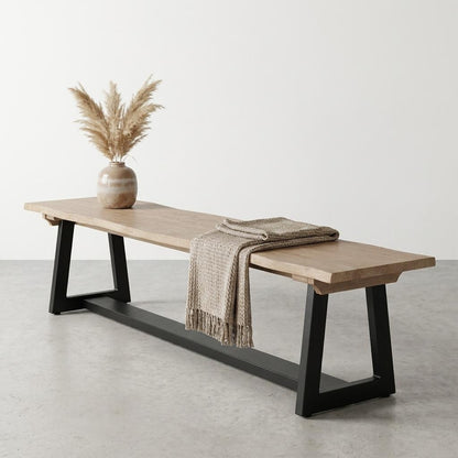 Wooden bench with black legs, draped throw, and vase with pampas grass.