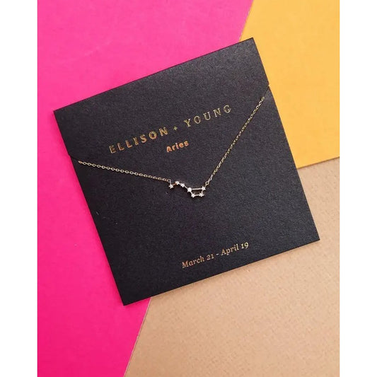 Gold Aries constellation necklace on a vibrant pink and yellow background.