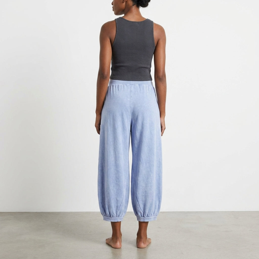 Woman in a black tank top and blue pants, standing barefoot, facing away.