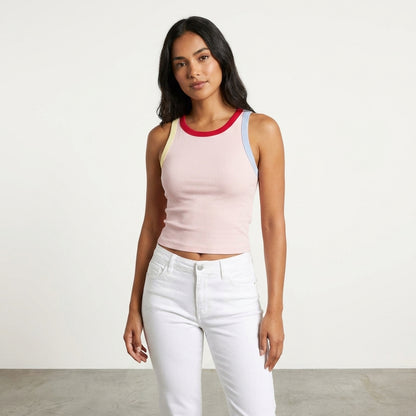 Woman in a colorful tank top and white pants against a plain background.