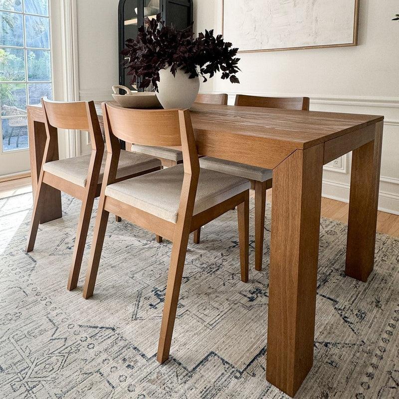 Wood dining table with four chairs and a vase on a patterned rug.