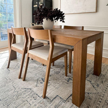 Wood dining table with four chairs and a vase on a patterned rug.