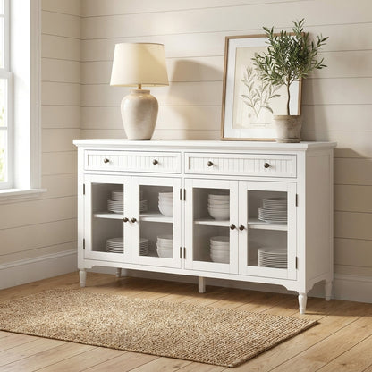 White sideboard with a lamp, plant, and art, on wooden floor with a rug.