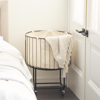 Wire laundry basket with beige fabric and a textured blanket.
