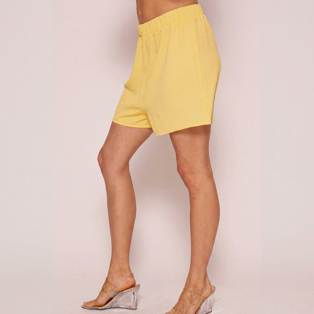 Person in yellow shorts and clear-heeled mules, side view.