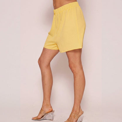 Person in yellow shorts and clear-heeled mules, side view.