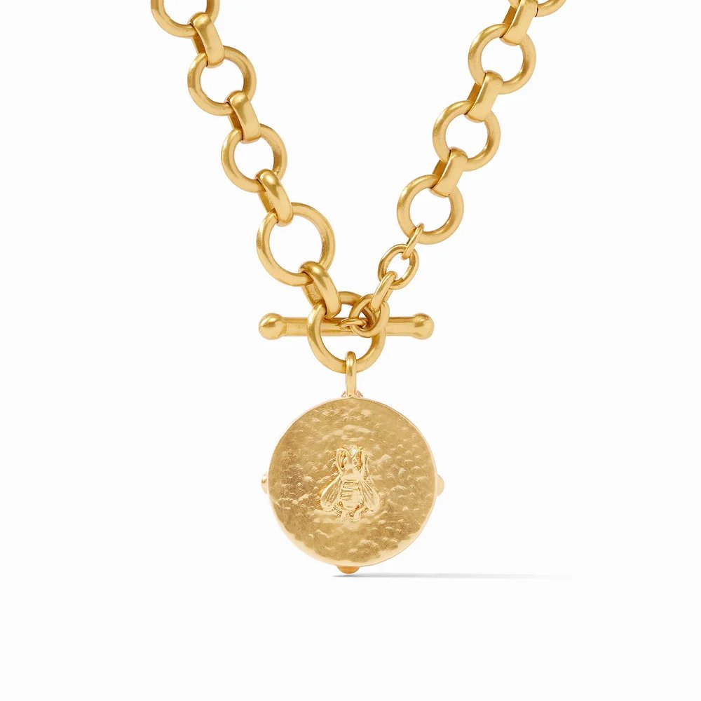 A gold chain necklace with a hammered round pendant and toggle clasp.
