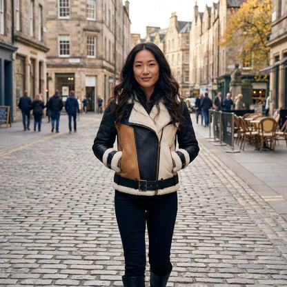 A woman in a shearling jacket stands on a cobblestone street lined with historic buildings.