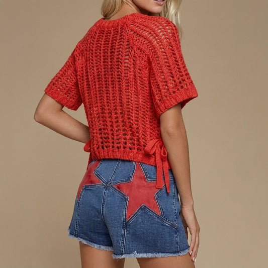 Woman in a red knit top and star-patterned denim shorts.