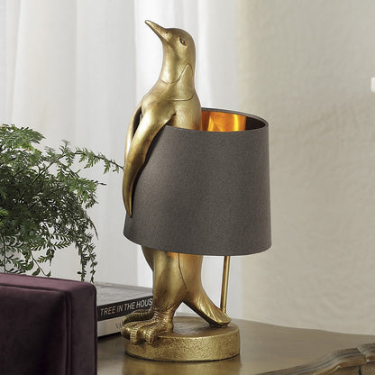 Gold penguin lamp with a dark shade on a table.