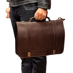 Person holding a brown leather briefcase, wearing a dark jacket and jeans.