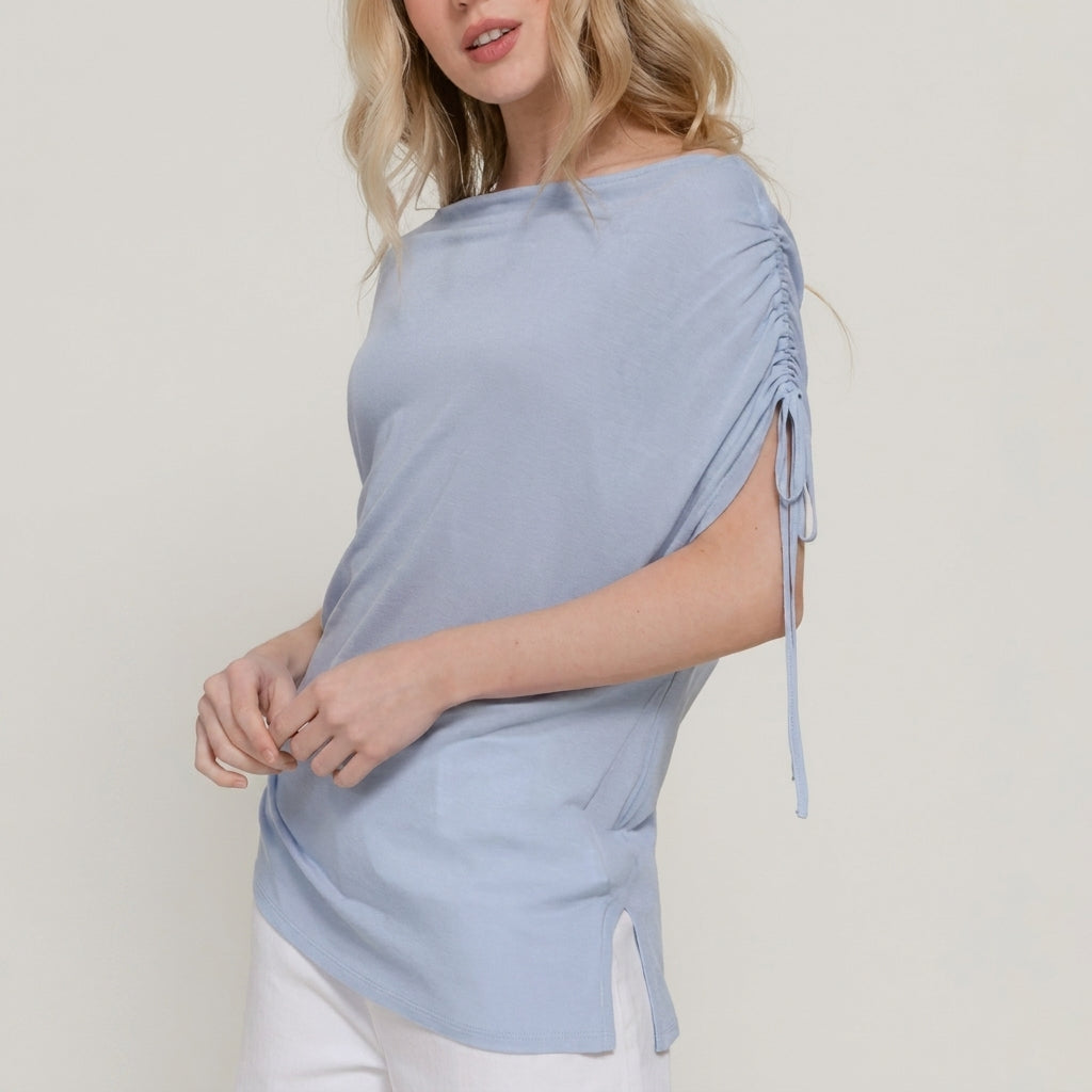 Woman wearing a light blue ruched sleeve top with white pants.