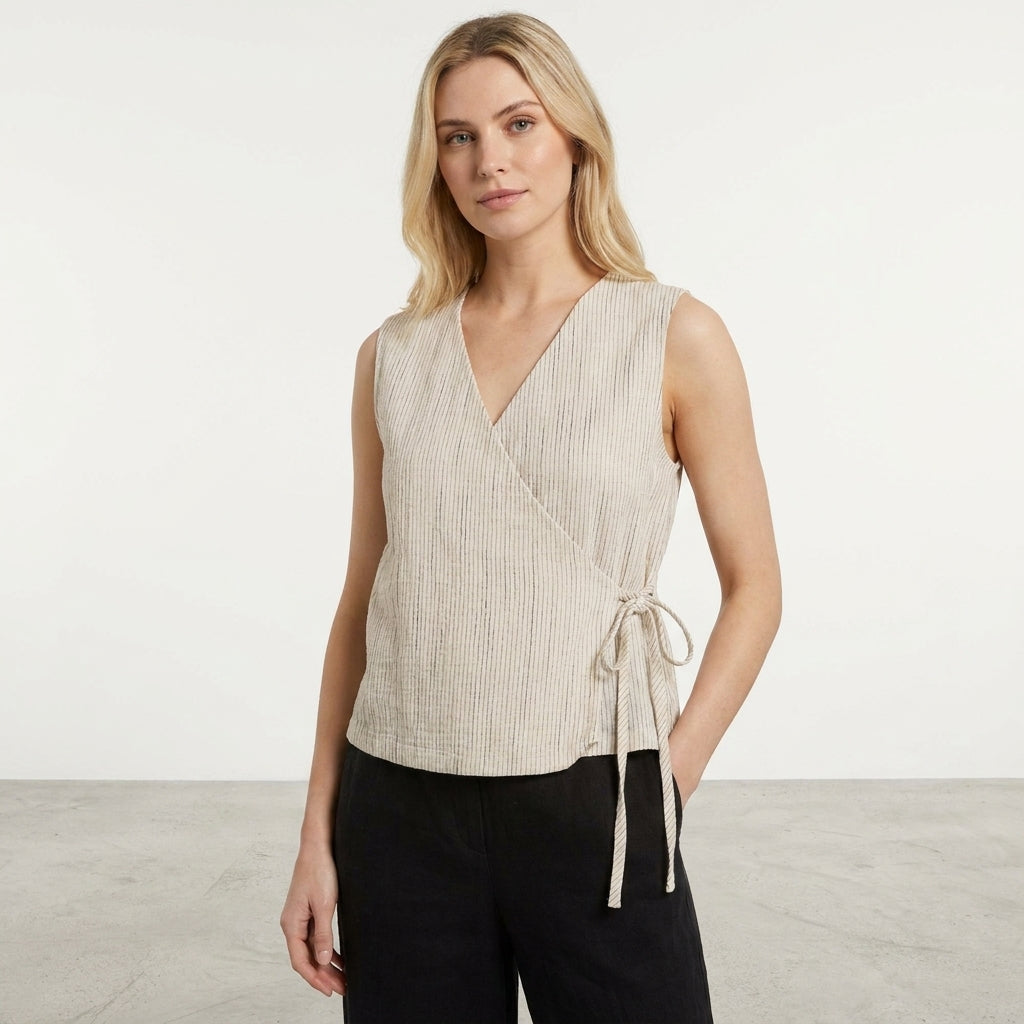 Woman in a sleeveless beige wrap top and black pants in a minimal setting.