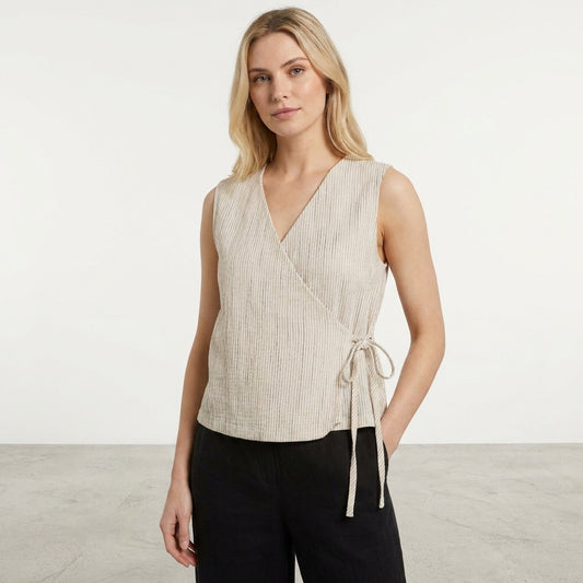 Woman in a sleeveless beige wrap top and black pants in a minimal setting.